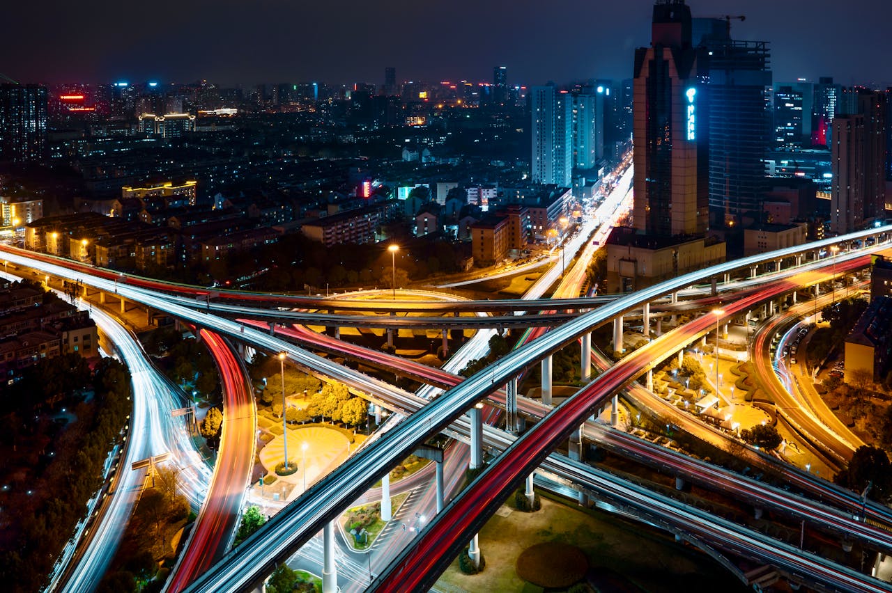 Dynamic aerial night view of a city with illuminated highway interchange and skyscrapers.