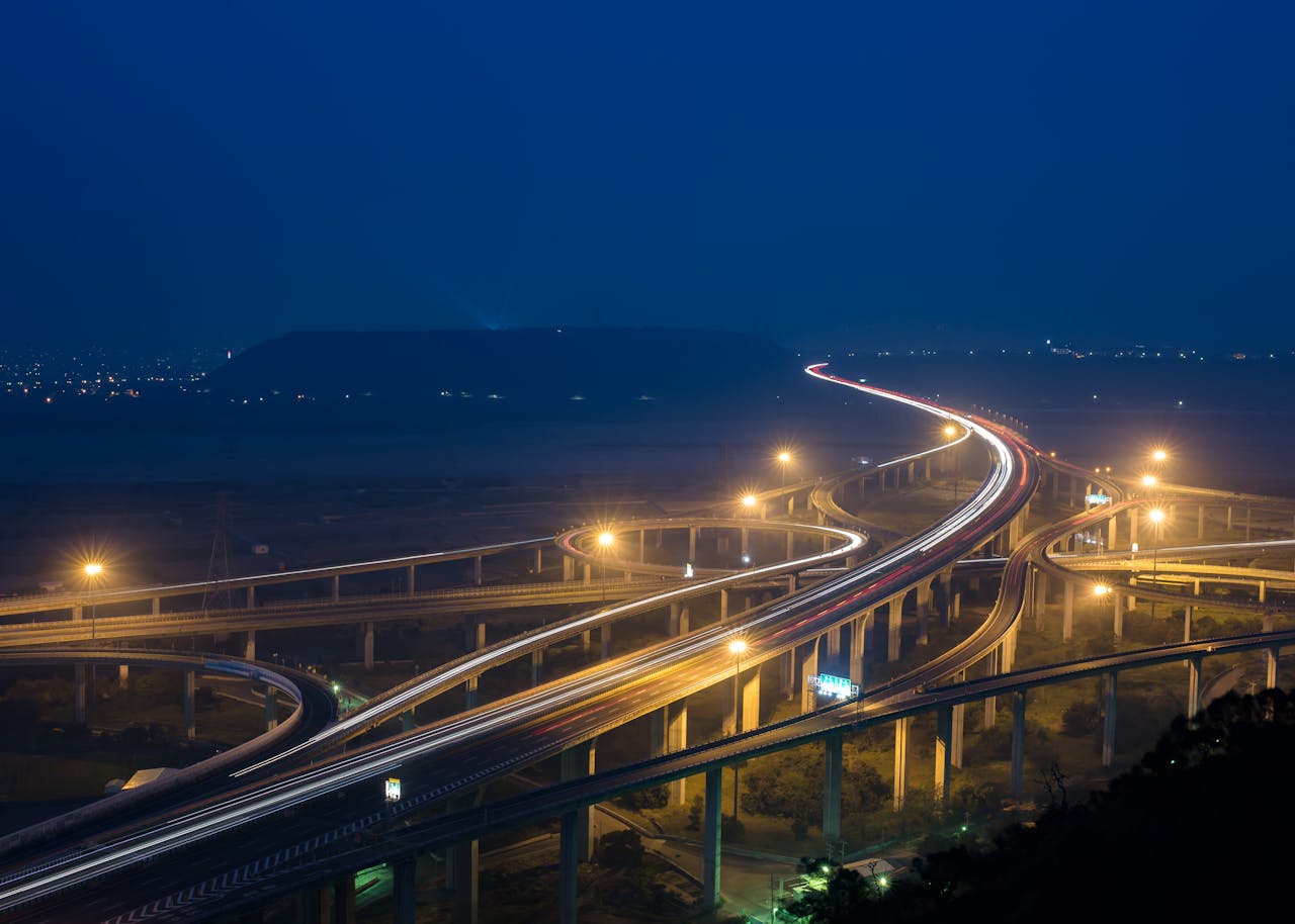 Aerial view of a night highway interchange with long exposure light trails and illuminated structure.